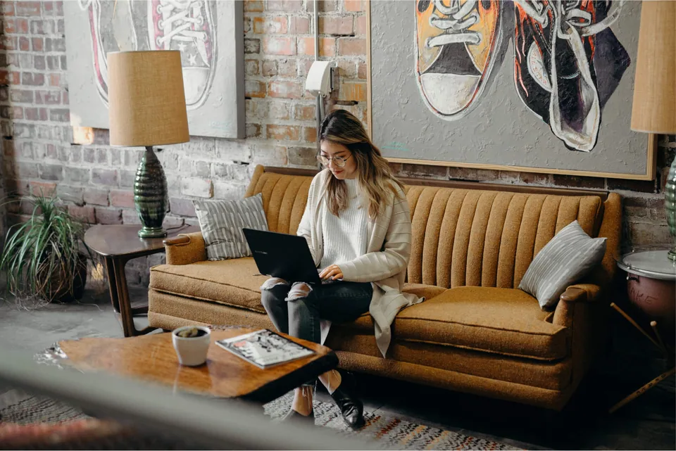 A woman sitting on a coach with a laptop.