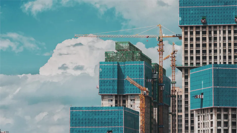 Two buildings under construction with cranes and blue sky in the background.